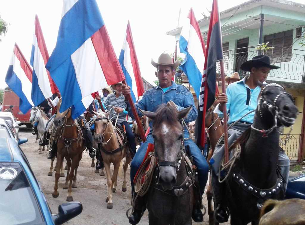 Jinetes a caballo portando la bandera de la patria